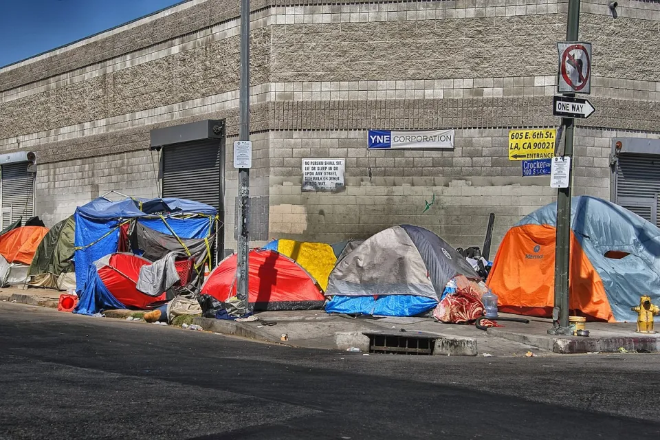 Tents inhabited by unhoused people lined up on sidewalk in Los Angeles, California in front of industrial building.